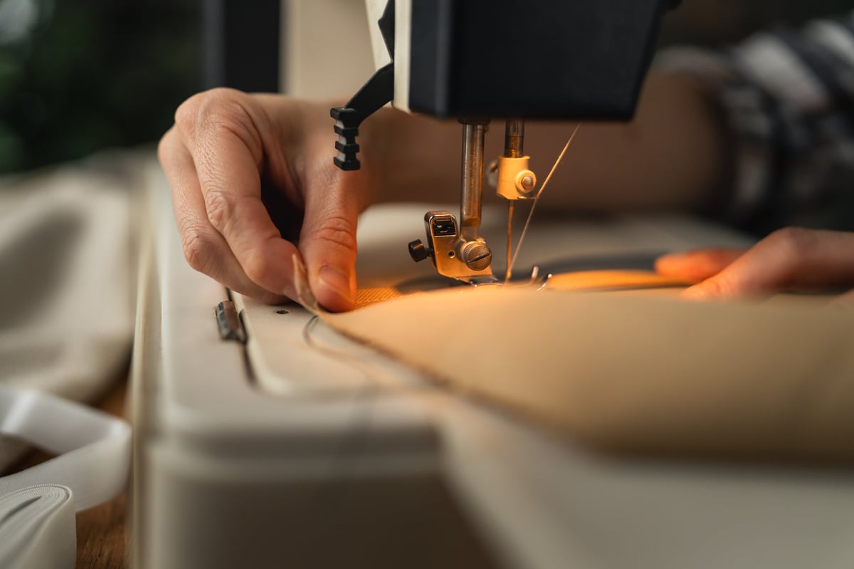 Hands guiding fabric under sewing machine during alteration